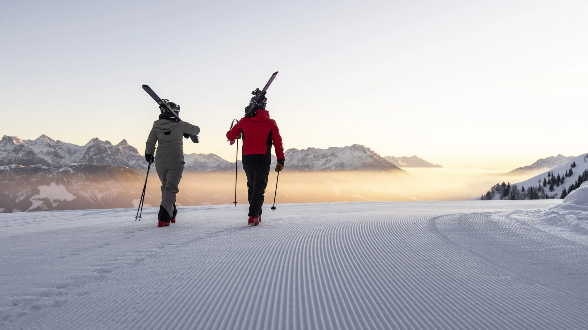 Zwei Skitourengeher mit geschulterten Ski auf einer frisch präparierten Piste
