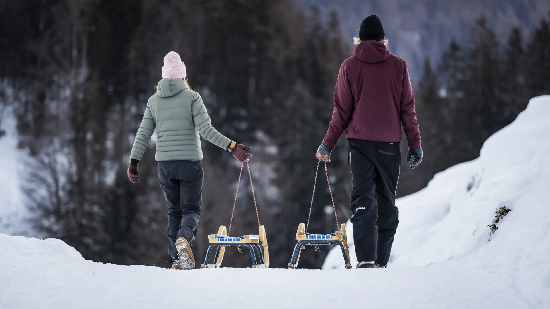 Zwei Personen mit Rodeln auf einem verschneiten Waldweg